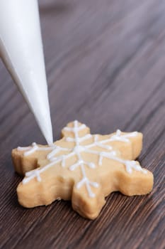 Close up of drawing gingerbread Christmas snowflake sugar cookie on wooden table background with white icing, concept of holiday celebration.