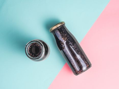 Detox activated charcoal black chia water or mocktail on colorful blue and pink background.Two bottle with black chia infused water.Detox drink idea and recipe.Vegan food and drink.Top view