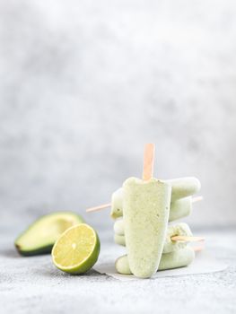 Homemade raw vegan avocado lime popsicle. Sugar-free, non-dairy green ice cream on gray cement textured background. Copy space. Ideas and recipes for healthy snack, dessert or smoothie. Vertical