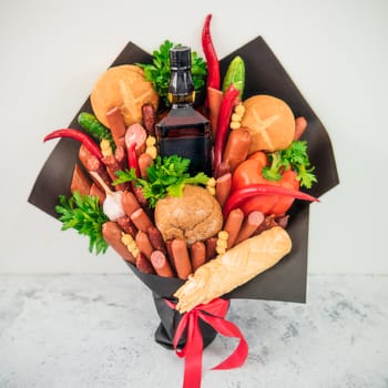 Meat and chese bouquet for man. Eating bouquet on gray background. Sausages, vegetables, cheese, bread and strong alcohol bottle in bouquet. Unusual gift for brutal man.