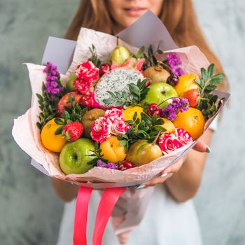 Fruit and berries bouquet. Eating bouquet in female hands. Apple, orange, strawberry, pear, kiwi, dragon fruit and flowers, eucalyptus. Shallow DOF
