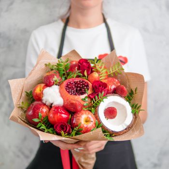 Fruit and berries bouquet. Eating bouquet in female hands. Pomegranate, strawberry, apples, coconut and roses flowers, eucalyptus. Shallow DOF