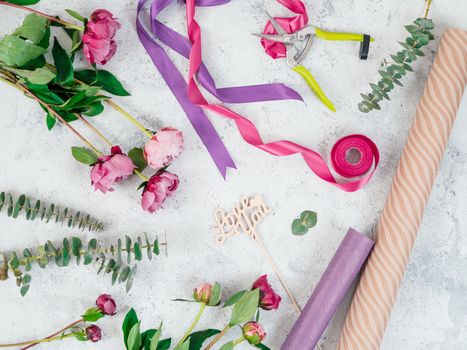 Floristic flat lay. Flowers, wrapping paper, ribbons and Love you wooden sign on gray tabletop. Roses, eucalyptus, Copy space. Can use for social media posting