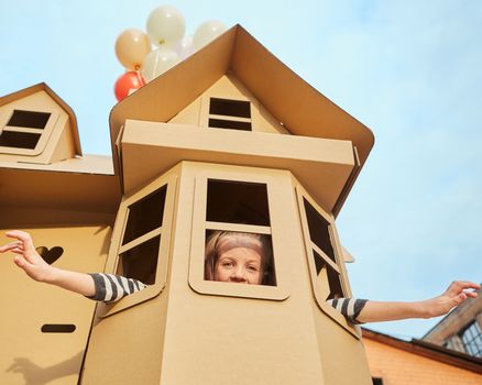 Child playing in a cardboard playhouse. Eco concept.