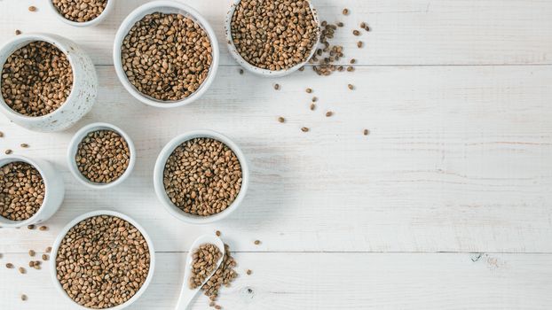 Hemp seeds in small white bowls and spoon on white wooden table. Set of small bowls with raw organic unrefined hemp seed. Superfood and vegan concept. Top view or flat lay.Copy space for text. Banner