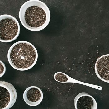 Organic chia seeds on black tabletop. Set of small bowls with organic chia seed. Superfood concept. Copy space. Top view or flat-lay.