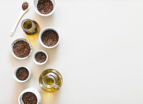 flax seeds and flaxseed oil on white or light beige background. Set of small bowls with organic flax seed or linen seed. Flax oil is rich in omega-3 fatty acid. Copy space. Top view or flat-lay.