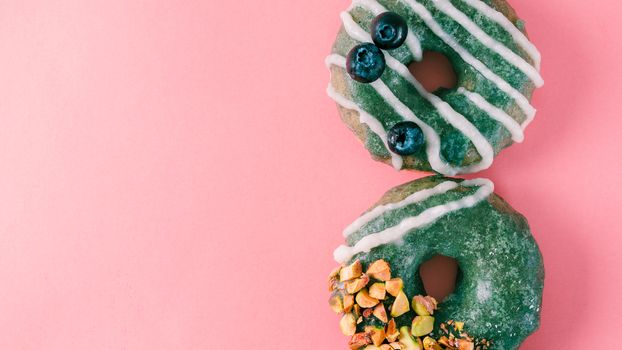 Vegan doughnuts with chia seeds topped with healthy spirulina glaze with pistachio and blueberry. Blue green spirulina donuts on pink background. Copy space. Top view. Banner