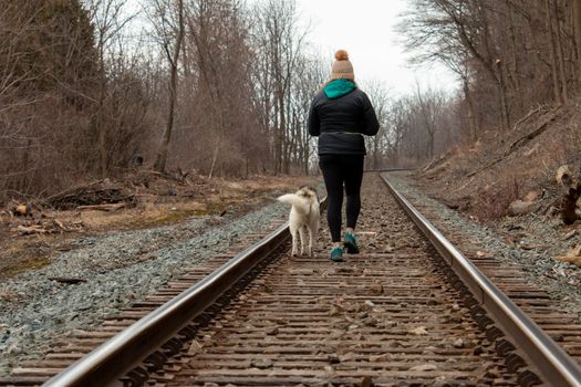 Hamilton Ontario, March 24 2020: Editorial photo of a women walking on train tracks with her dog. Editorial theme of loneliness . High quality photo