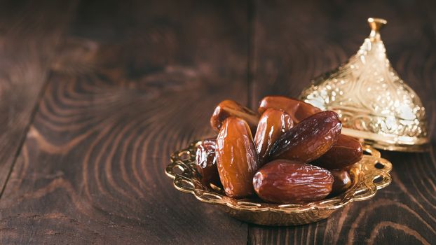 Metal plate of sweet organic dates on dark wooden table. Dried dates with copy space for text. Banner.