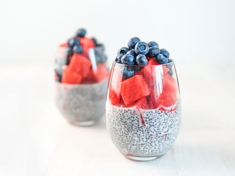 Healthy breakfast concept and idea - chia pudding with watermelon and blueberries. Two glass with chia pudding dressed watermelon and blueberry on white wooden tabletop. Copy space for text.