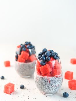 Healthy breakfast concept and idea - chia pudding with watermelon and blueberries. Two glass with chia pudding dressed watermelon and blueberry on white wooden tabletop. Copy space for text. Vertical.