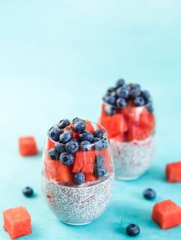 Healthy breakfast concept and idea - chia pudding with watermelon and blueberries. Two glass with chia pudding dressed watermelon and blueberry on blue background. Copy space for text. Vertical.