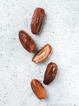 Sweet raw dates on gray cement background. Whole dates and half with bone date on grey concrete surface. Sugar free alternatives concept with space for text. Top view or flat-lay. Vertical.