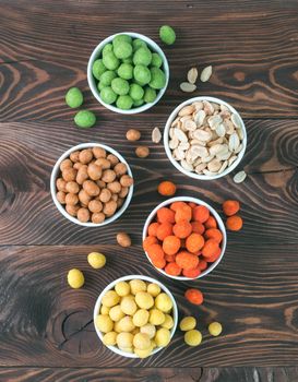 Assortment of different peanuts snack for beer, wine, party. Salted peanuts, peanuts in coconut glaze, green vasabi, red spicy chilli, yellow cheese glaze on brown wooden table. Copy space. Vertical.