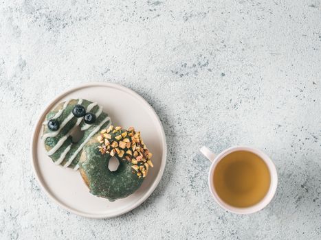 Vegan doughnuts with chia seeds topped with healthy spirulina glaze with pistachio and blueberry. Blue green spirulina donuts and herbal tea cup on gray background, top view or flat lay. Copy space