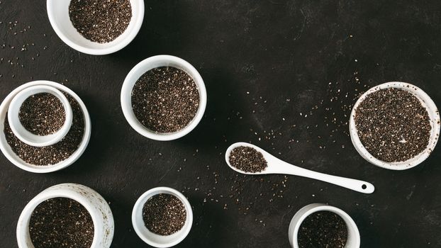Organic chia seeds on black tabletop. Set of small bowls with organic chia seed. Superfood concept. Copy space. Top view or flat-lay.