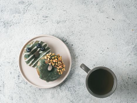 Vegan doughnuts with chia seeds topped with healthy spirulina glaze with pistachio and blueberry. Blue green spirulina donuts and tea cup on gray background, top view or flat lay. Copy space