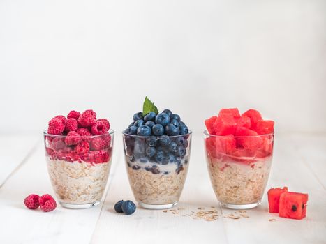 Healthy breakfast: overnight oats with fresh fruits and berries in glass. Overnight oatmeal porridge with watermelon, raspberry, blueberry,decorated mint. Overnight oats on white background,copy space