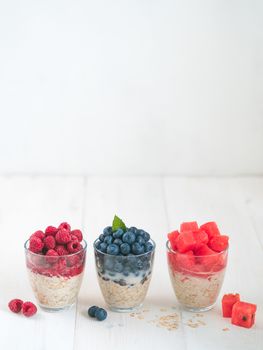 Healthy breakfast:overnight oats with fresh fruits and berries in glass.Overnight oatmeal porridge with watermelon,raspberry,blueberry,decorated mint. Overnight oats on white table,copy space.Vertical