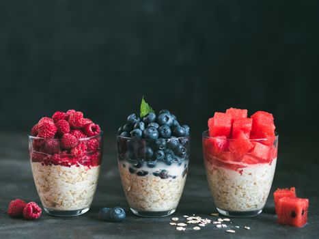 Healthy breakfast: overnight oats with fresh fruits and berries in glass. Overnight oatmeal porridge with watermelon, raspberry, blueberry,decorated mint. Overnight oats on black background,copy space