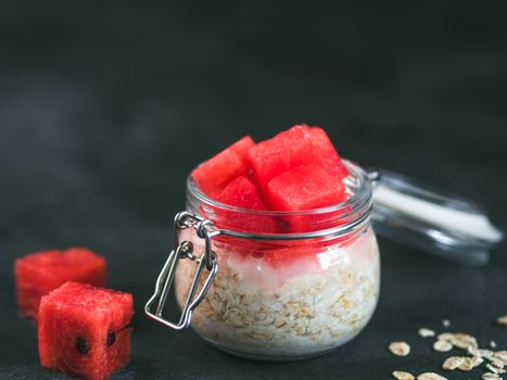 Healthy breakfast: overnight oats with watermelon pieces in glass jar. Overnight oatmeal porridge with watermelon. Overnight oats on black background. Copy space for text.