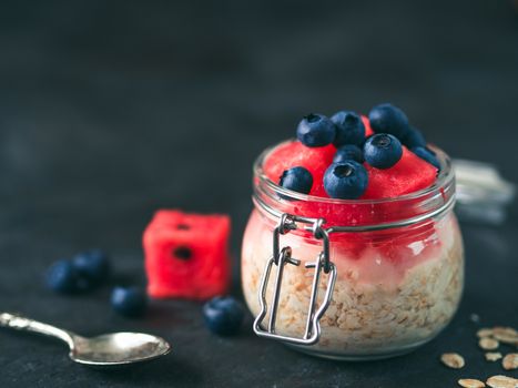 Healthy breakfast idea and recipe: overnight oats with fresh fruits and berries in glass jar.Overnight oatmeal porridge with watermelon,blueberry.Overnight oats on black background.Copy space for text