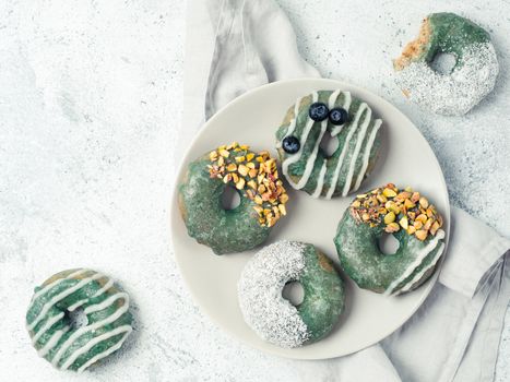 Vegan doughnuts with chia seeds topped with healthy spirulina glaze with pistachio, desiccated coconut and blueberry. Blue green spirulina donuts on gray background. Top view. Copy space.