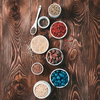 Various superfoods in small bowl on wooden table.Selection super food.Superfood as blueberry, chia, raw cocoa bean, goji, hemp seeds, quinoa, brown rice.Copy space for text.Top view or flat lay.Square