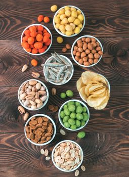 Assortment of different snack for beer, wine, party. Peanuts in coconut glaze, green vasabi, red spicy chilli, yellow cheese glaze, chips, pistachio, crackers, fish on brown wooden table. Copy space