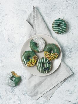 Vegan doughnuts with chia seeds topped with healthy spirulina glaze with pistachio, desiccated coconut and blueberry. Blue green spirulina donuts on gray background. Top view. Copy space. Vertical.