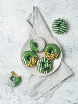 Vegan doughnuts with chia seeds topped with healthy matcha tea glaze with pistachio, desiccated coconut and blueberry. Green matcha tea donuts on gray background. Top view. Copy space. Vertical.