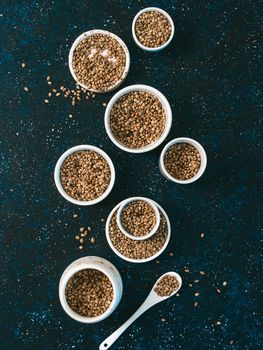 Hemp seeds in small white bowls and spoon on dark blue tabletop. Set of small bowls with raw organic unrefined hemp seed. Superfood and vegan concept. Top view or flat lay.Copy space for text.Vertical