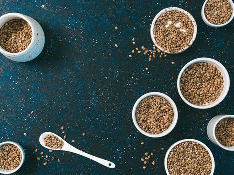 Hemp seeds in small white bowls and spoon on dark blue tabletop. Set of small bowls with raw organic unrefined hemp seed. Superfood and vegan concept. Top view or flat lay.Copy space for text.