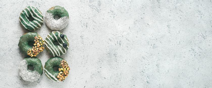 Vegan doughnuts with chia seeds topped with spirulina glaze with pistachio, coconut and blueberry. Blue green spirulina donuts on gray background, top view or flat lay. Copy space for text. Banner