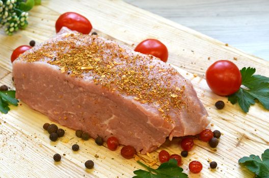 Raw pork meat on cutting board and vegetables and greens.