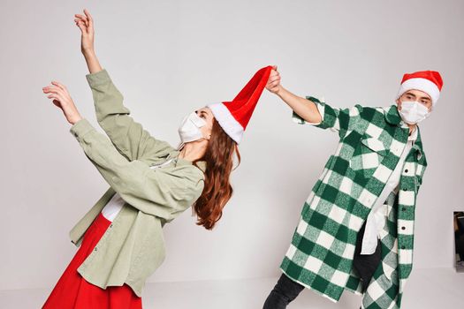 young couple celebrate Christmas together in santa hat emotions medical masks on face. High quality photo