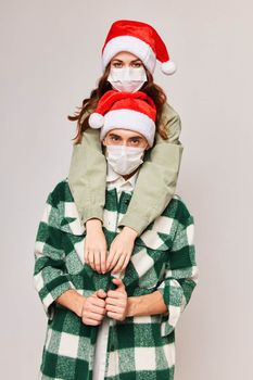 Man and woman in Christmas hats embrace holiday medical masks. High quality photo