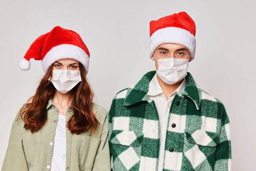 A man and a woman in New Year's Santa hats are standing side by side in medical masks. Close-up protection. Studio. High quality photo