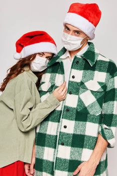 young couple in christmas hats medical masks on their face hugs holiday. High quality photo