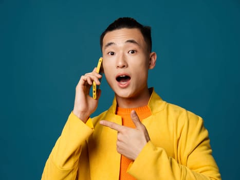A Korean man is talking on the phone and pointing to the side against a blue background Copy Space. High quality photo