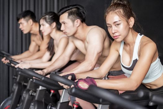 Young woman and friends on fitness bike in gym during workout