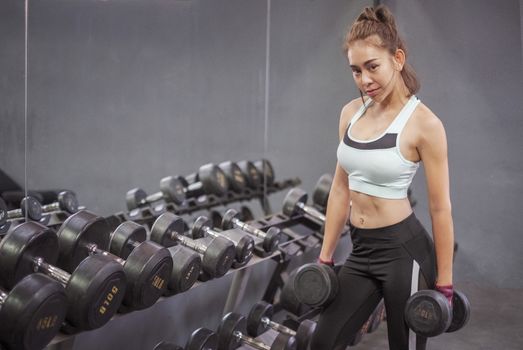 Young healthy woman lifting dumbbells in fitness gym
