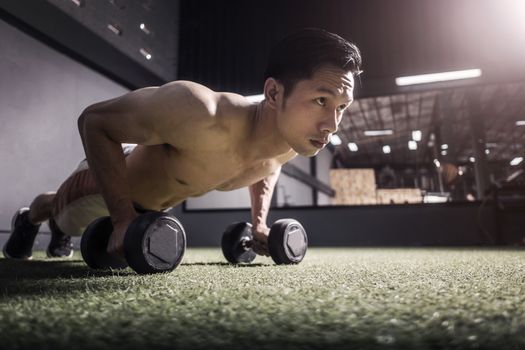 Strong fitness man doing arm workout with dumbbells in the gym