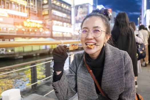 Young woman tourists enjoy eating street food in walking at street shopping center Dotonbori in Osaka, Japan.