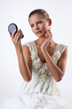 Young beautiful woman applying cosmetics onto her face