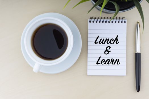 LUNCH AND LEARN text with fountain pen, notepad, and decorative flower on wooden background. Business and copy space concept.

