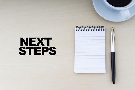NEXT STEPS text with fountain pen and cup of coffee on wooden background.Business and copy space concept.
