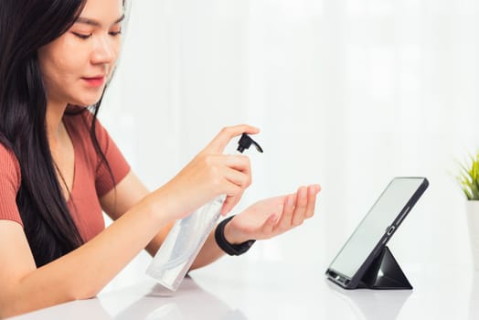 Asian Business young woman working from home office he quarantines disease coronavirus or COVID-19 her cleaning hands with sanitizer gel on front tablet computer