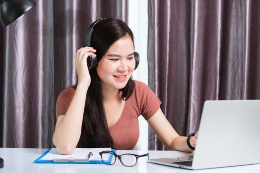 Work from home, Asian young businesswoman smile wearing headphones video conference call or facetime by laptop computer meeting with team on desk at home office